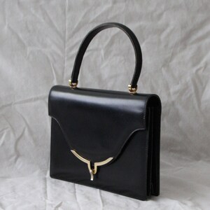 May include: A black leather handbag with a gold-toned handle and clasp. The bag has a rectangular shape and a flap closure.
