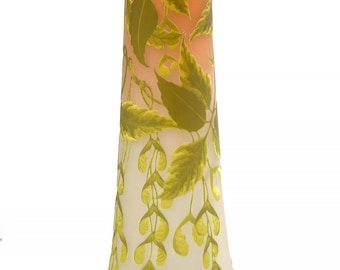 Könnte beinhalten: Eine hohe, schlanke Vase mit ausgestelltem Boden, die einen Farbverlauf von Pfirsich bis Weiß aufweist. Die Vase ist mit grünen Blättern und gelben Samenkapsel-Designs verziert. Das Gesamtdesign erinnert an den Jugendstil.