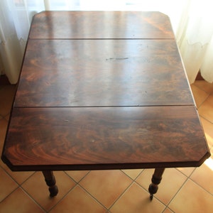 Puede incluir: Una mesa de madera marr&oacute;n oscuro con un dise&ntilde;o de hoja ca&iacute;da. La mesa tiene una tapa rectangular con dos hojas que se pueden extender. La mesa tiene cuatro patas y est&aacute; hecha de madera maciza.