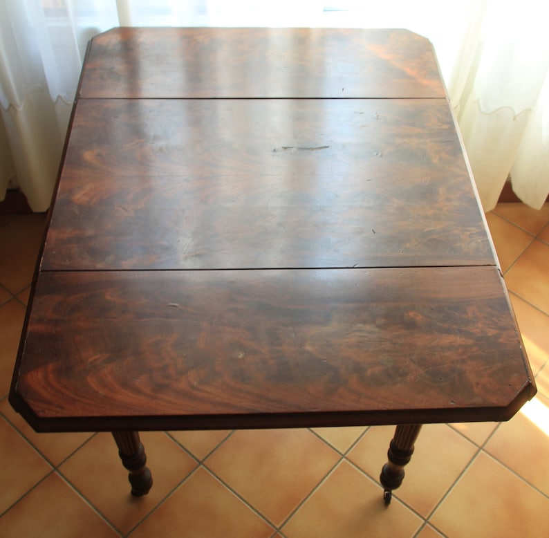 Puede incluir: Una mesa de madera marr&oacute;n oscuro con un dise&ntilde;o de hoja ca&iacute;da. La mesa tiene una tapa rectangular con dos hojas que se pueden extender. La mesa tiene cuatro patas y est&aacute; hecha de madera maciza.
