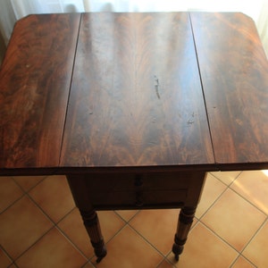 Puede incluir: Una mesa de madera marr&oacute;n oscuro con un dise&ntilde;o de hoja ca&iacute;da. La mesa tiene dos cajones y cuatro patas torneadas. La mesa est&aacute; en buen estado y tiene una hermosa p&aacute;tina.