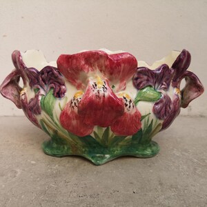 Puede incluir: Un cuenco floral de cerámica con interior crema y base verde. El exterior está adornado con iris pintados a mano en tonos rojos, morados y verdes. El cuenco tiene asas a cada lado. Aproximadamente 25 cm de largo.