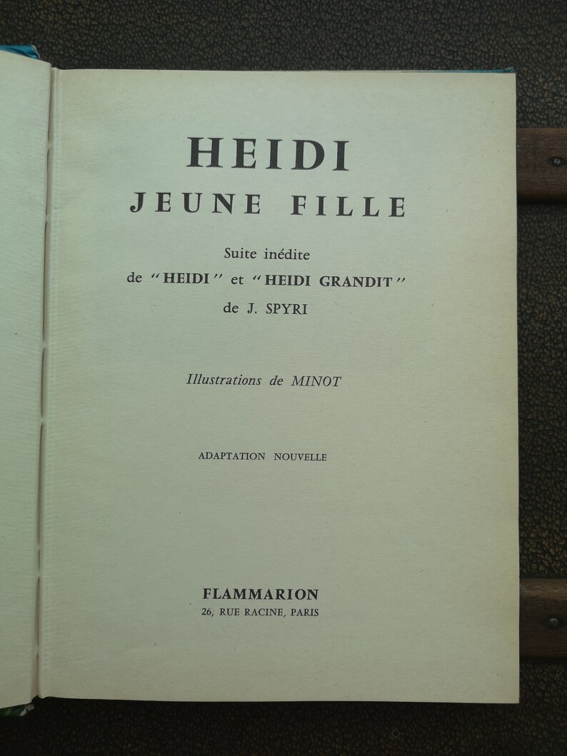 May include: A book cover with the title "HEIDI JEUNE FILLE" in black text on a white background. The subtitle is "Suite in&eacute;dite de "HEIDI" et "HEIDI GRANDIT" de J. SPYRI". The book cover also includes the text "Illustrations de MINOT" and "ADAPTATION NOUVELLE". The publisher is "FLAMMARION 26, RUE RACINE, PARIS".