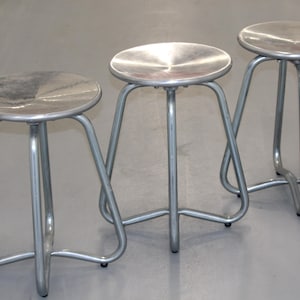 May include: Three silver metal stools with round seats. The stools have a simple, modern design and are made of sturdy metal.