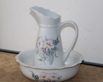 May include: White porcelain pitcher and bowl set with a floral design. The pitcher has a handle and a scalloped rim. The bowl has a scalloped rim and a floral design.