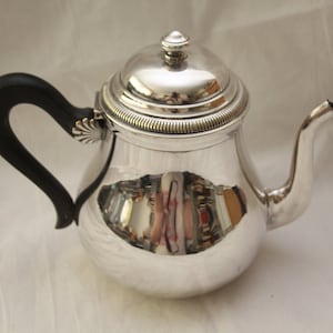 Peut inclure: Une théière en argent avec une poignée noire et une surface brillante et réfléchissante. La théière a un corps rond et un couvercle avec un bouton sur le dessus.