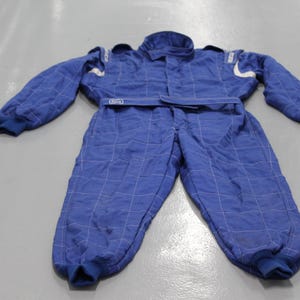 May include: Blue racing suit with white accents and a quilted pattern. The one-piece suit has long sleeves, a collar, and a belt. The suit is designed for motorsports and racing.