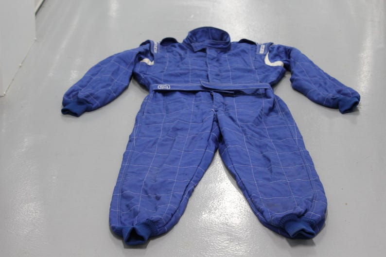 May include: Blue racing suit with white accents and a quilted pattern. The one-piece suit has long sleeves, a collar, and a belt. The suit is designed for motorsports and racing.