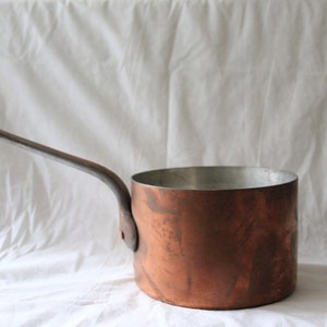 May include: A copper saucepan with a long, silver handle. The saucepan has a slightly tarnished finish.