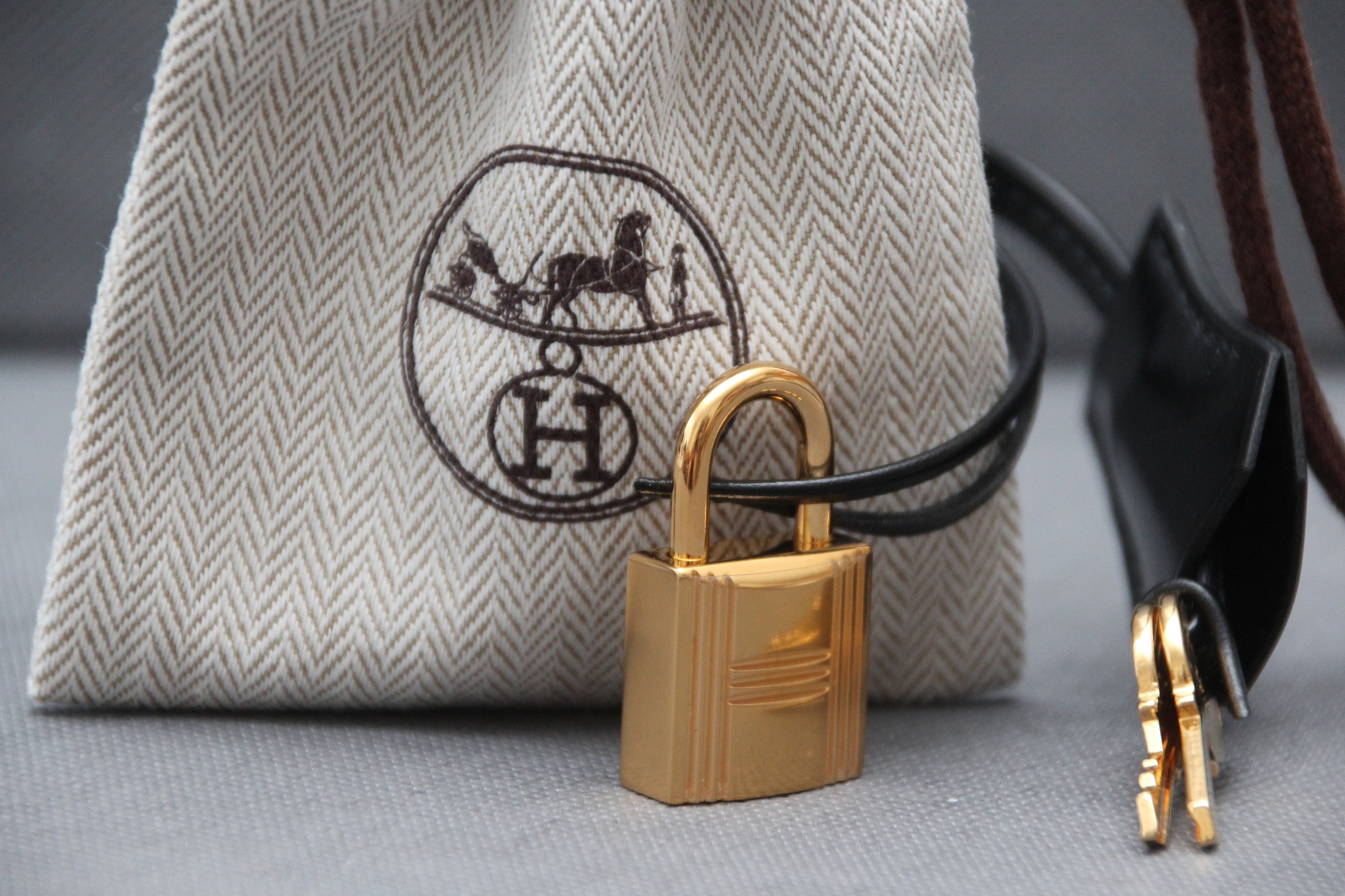 A black birkin bag with gold details by Hermes and black slides