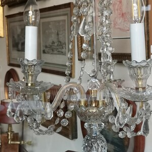 May include: A clear crystal chandelier with three candle-style lights. The chandelier has hanging crystal accents and a decorative base. The lights have a flame-shaped design. The fixture is likely vintage or antique.
