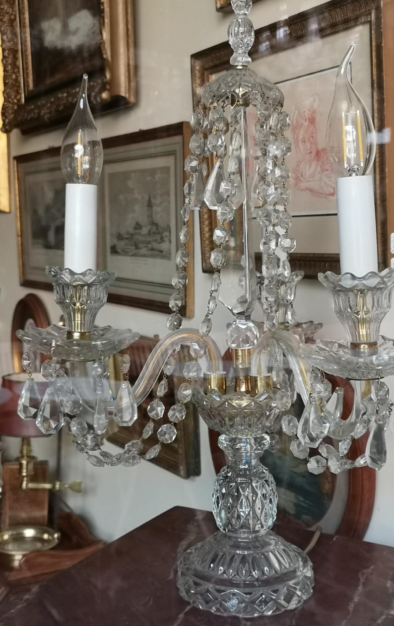 May include: A clear crystal chandelier with three candle-style lights. The chandelier has hanging crystal accents and a decorative base. The lights have a flame-shaped design. The fixture is likely vintage or antique.