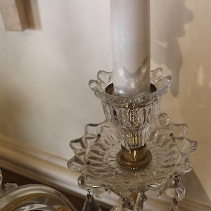 May include: A vintage crystal chandelier with a white candle-shaped light bulb. The chandelier has a clear, patterned glass base with a gold-coloured metal accent. Decorative crystal pendants hang from the base.