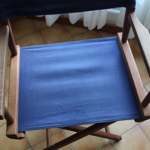 May include: A blue canvas director's chair with wooden arms and legs. The chair is folded and sitting on a tiled floor.
