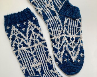 Könnte beinhalten: Ein Paar gestrickte Socken mit geometrischem Muster. Die Socken haben einen dunkelblauen Bund, eine Ferse und eine Spitze, mit einem weißen und blauen Design auf dem Hauptteil. Die Socken sind aus weichem, strukturiertem Garn gefertigt.