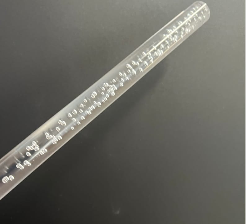 May include: A clear plastic wand with small air bubbles embedded throughout. The wand is approximately 12 inches long.