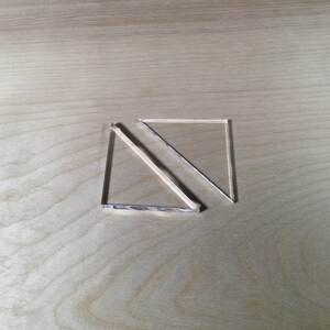 May include: Two clear acrylic triangles, one overlapping the other, on a light wood surface.