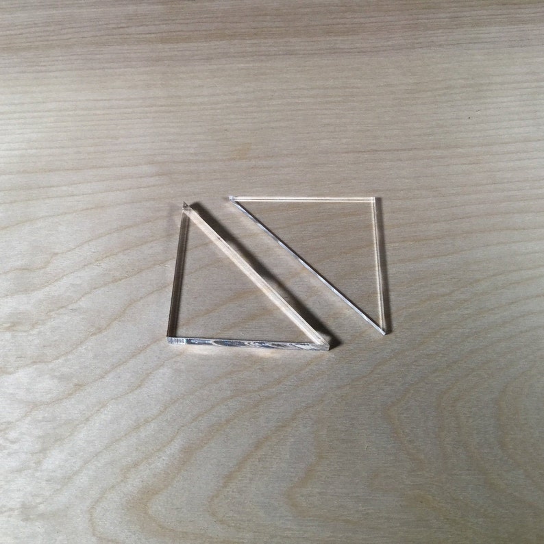 May include: Two clear acrylic triangles, one overlapping the other, on a light wood surface.