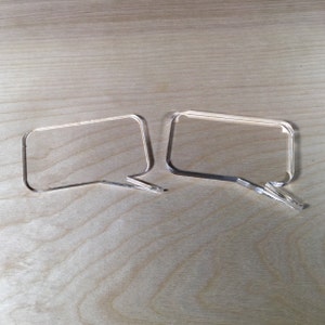 May include: Two clear acrylic speech bubbles, one slightly larger than the other, are placed side-by-side on a light brown wooden surface.