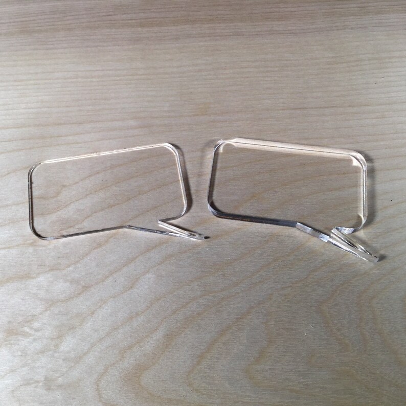May include: Two clear acrylic speech bubbles, one slightly larger than the other, are placed side-by-side on a light brown wooden surface.
