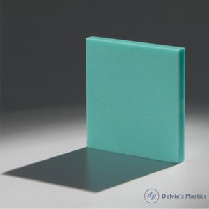 May include: A rectangular, teal-colored acrylic sheet stands upright, casting a shadow on a white surface. The sheet has a textured appearance and is illuminated from the side, creating a contrast between light and shadow. The bottom right corner has the text "Delvie's Plastics".