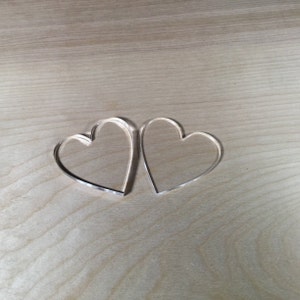 May include: Two clear acrylic heart shapes on a light brown wooden surface.
