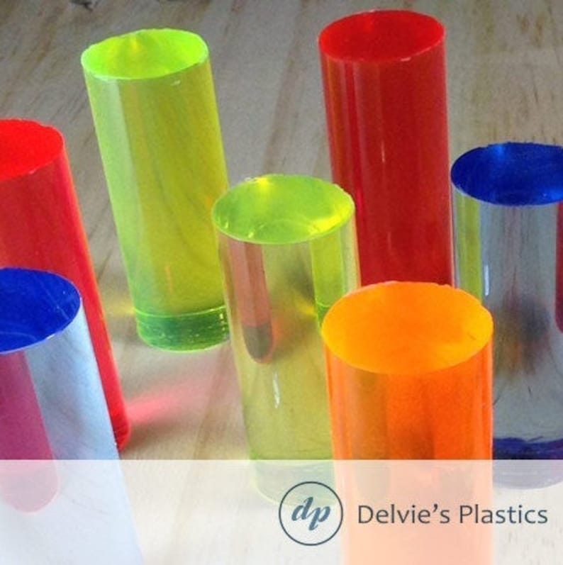 May include: Assortment of colorful acrylic rods in various colors, including red, yellow, orange, blue, and green. The rods are clear and translucent, allowing light to pass through them. The rods are arranged in a row on a wooden surface.