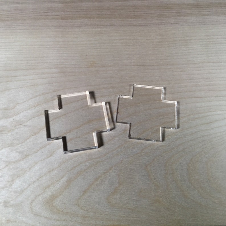 May include: Two clear plastic cross-shaped stencils on a light wood surface.