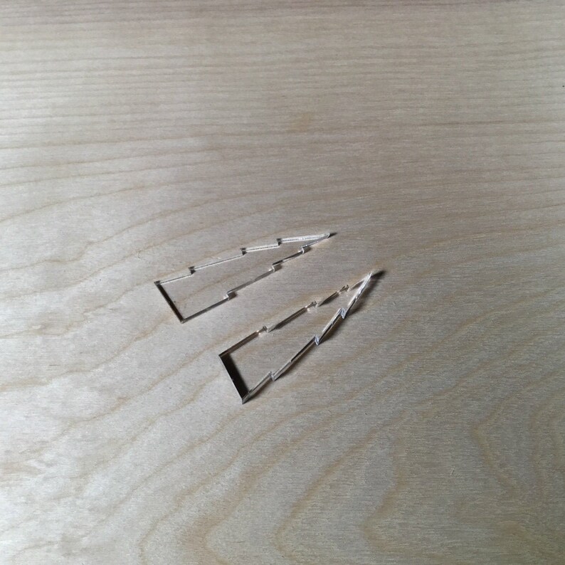 May include: Two laser cut wooden shapes in the form of a Christmas tree, on a light wood background.