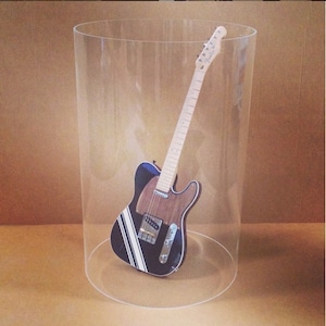 May include: A black and white electric guitar with a wooden body is displayed inside a clear acrylic cylinder.