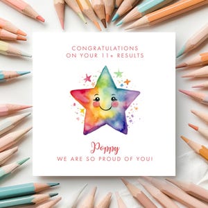 May include: A square greeting card featuring a watercolour rainbow star with a smiling face, surrounded by small colourful stars. The text reads: CONGRATULATIONS ON YOUR 11+ RESULTS, Poppy, WE ARE SO PROUD OF YOU! The card is framed by coloured pencils.