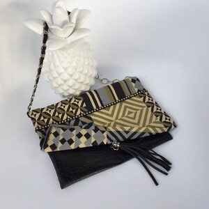Peut inclure: Une pochette à main à motif géométrique noir et or avec un rabat en cuir noir et un pompon noir. Le sac a une bandoulière en chaîne argentée.