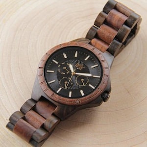 Op de afbeelding: Een houten polshorloge met een zwarte wijzerplaat en gouden accenten. Het horloge heeft een bruine houten band.