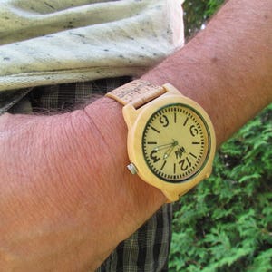 Puede incluir: Un reloj de pulsera de madera con una correa marr&oacute;n claro y una esfera marr&oacute;n claro. La esfera tiene n&uacute;meros y manecillas negros, y la palabra "PIM" est&aacute; impresa en el centro.