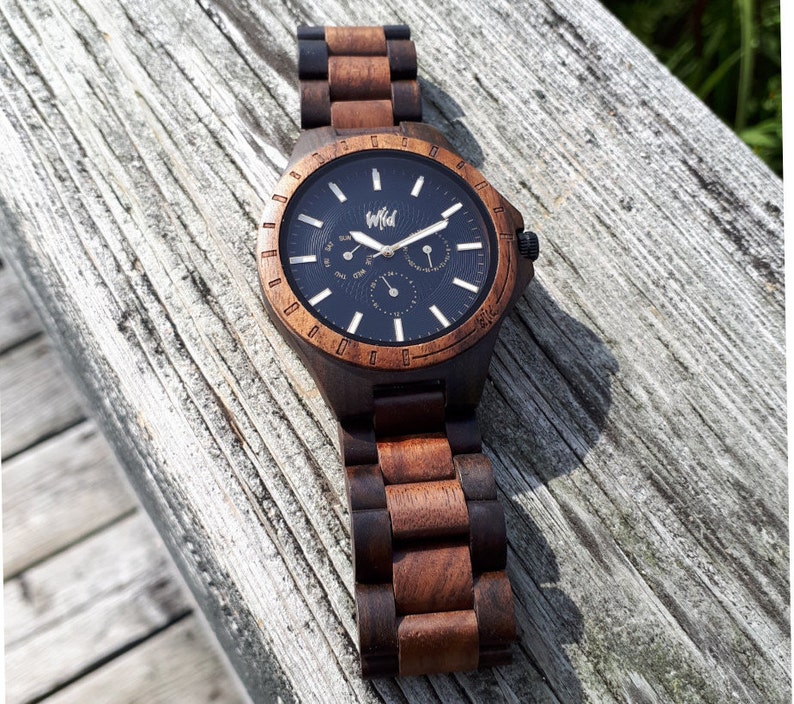 Op de afbeelding: Een bruin houten polshorloge met een zwarte wijzerplaat en witte wijzers. Het horloge heeft een chronograaffunctie en een datumscherm. Op de wijzerplaat van het horloge staat "Wild".