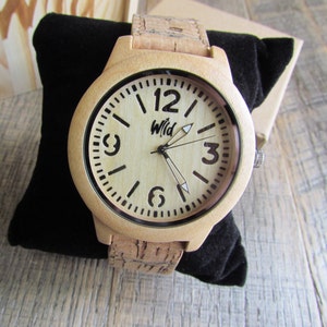 Puede incluir: Un reloj de pulsera de madera clara con una correa de corcho. La esfera del reloj es blanca con marcas negras y la palabra "Wild" impresa en negro.
