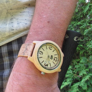 Puede incluir: Un reloj de pulsera de madera con una correa de corcho. La esfera del reloj es de color marr&oacute;n claro con marcas negras y fondo blanco. La esfera del reloj tiene agujas negras y la palabra "Myl" impresa en ella.