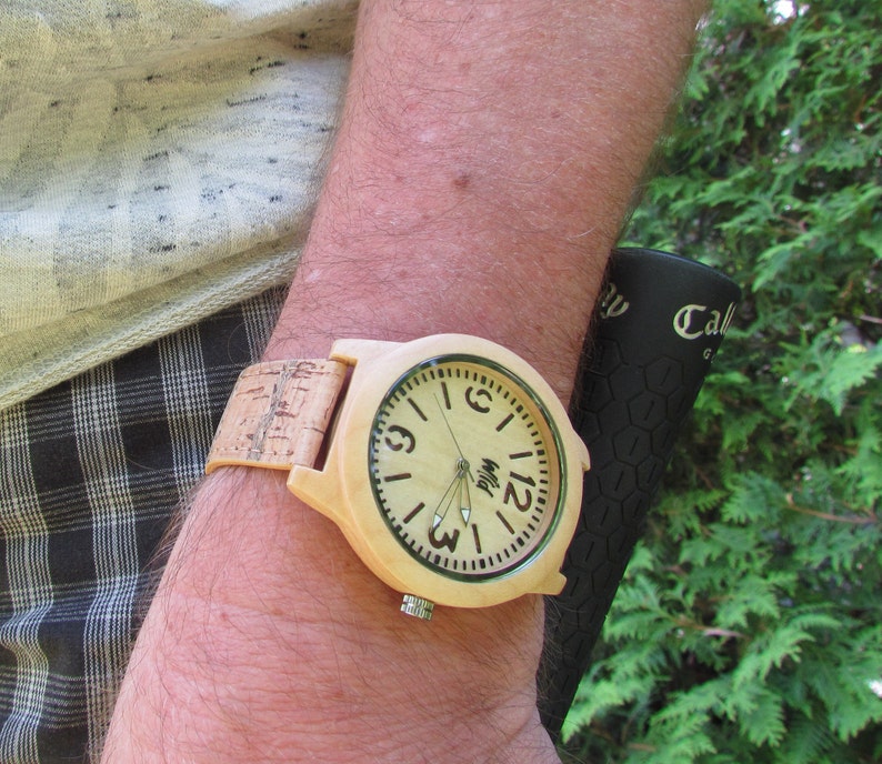 Puede incluir: Un reloj de pulsera de madera con una correa de corcho. La esfera del reloj es de color marr&oacute;n claro con marcas negras y fondo blanco. La esfera del reloj tiene agujas negras y la palabra "Myl" impresa en ella.