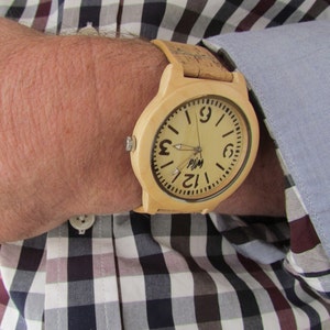 Puede incluir: Un reloj de pulsera de madera clara con una correa de corcho. La esfera del reloj es de color crema con n&uacute;meros y manecillas negros. La esfera del reloj tambi&eacute;n tiene la palabra "PJM" impresa.