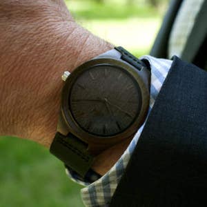 May include: A dark brown wooden wristwatch with a black leather band. The watch face has a dark wood grain pattern.