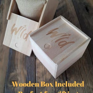 May include: Two wooden boxes with the word "Wild" engraved on them. The boxes are made of light wood and have a natural finish. The box on the left is open and has a burlap cushion inside. The boxes are perfect for gifting.