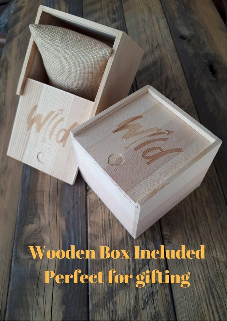 May include: Two wooden boxes with the word "Wild" engraved on them. The boxes are made of light wood and have a natural finish. The box on the left is open and has a burlap cushion inside. The boxes are perfect for gifting.