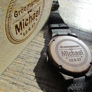 May include: A wooden watch with a black leather band. The back of the watch is engraved with the text "Groomsman Michael 12.6.17".