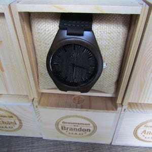 May include: Three wooden boxes with engraved names, "Michael", "Brandon", and "Andrew", each containing a black wooden wristwatch with a black face.