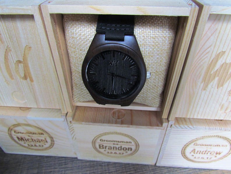May include: Three wooden boxes with engraved names, "Michael", "Brandon", and "Andrew", each containing a black wooden wristwatch with a black face.