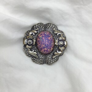 Puede incluir: Un broche de plata con una piedra de &oacute;palo p&uacute;rpura y rosa engastada en un dise&ntilde;o de filigrana.