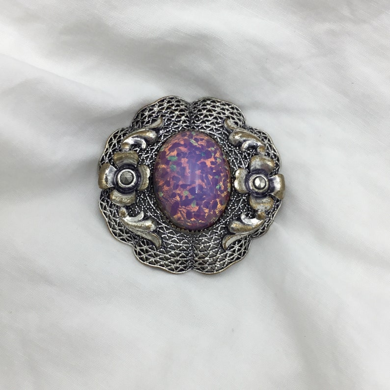 Puede incluir: Un broche de plata con una piedra de &oacute;palo p&uacute;rpura y rosa engastada en un dise&ntilde;o de filigrana.