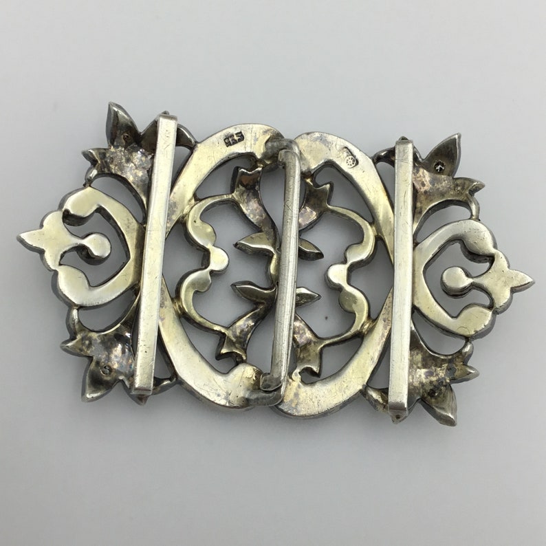 May include: Silver filigree buckle with a decorative design. The buckle is marked with the number "83" on the back.