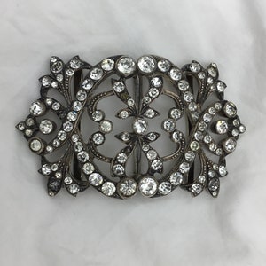 May include: A silver and crystal buckle with a floral design. The buckle is ornate and features a large number of small, clear crystals.