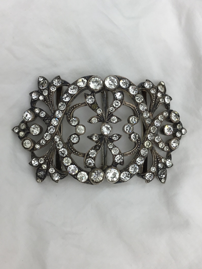 May include: A silver and crystal buckle with a floral design. The buckle is ornate and features a large number of small, clear crystals.